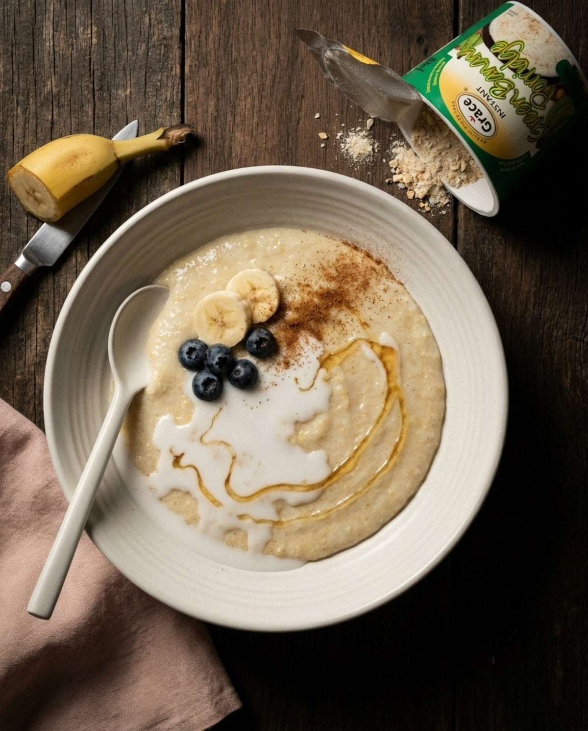 Grace Green Banana Porridge served with banana slices, blueberries, milk, and honey beside its open cup on a wooden table