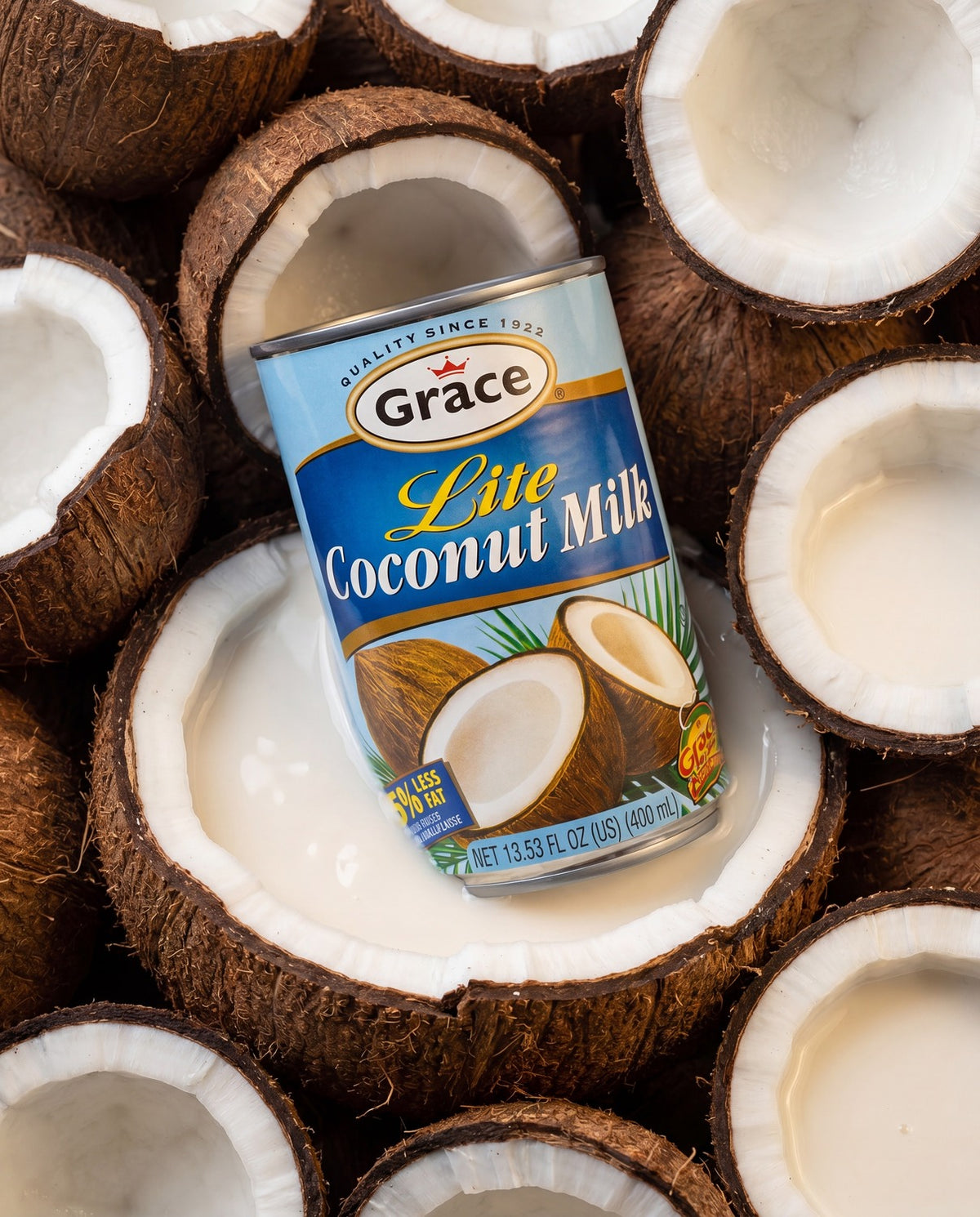 Angled view of Grace Lite Coconut Milk can with blue label and reduced fat claim, surrounded by halved coconuts