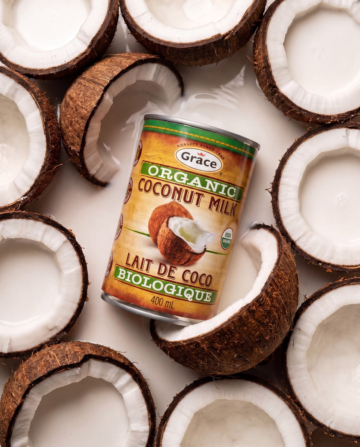 Angled can of Grace Organic Coconut Milk showcasing the 400 ML size surrounded by halved coconuts