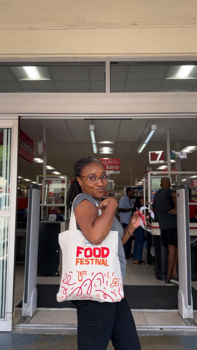Woman posing with a tote bag reading ‘FOOD FESTIVAL’ at a supermarket entrance