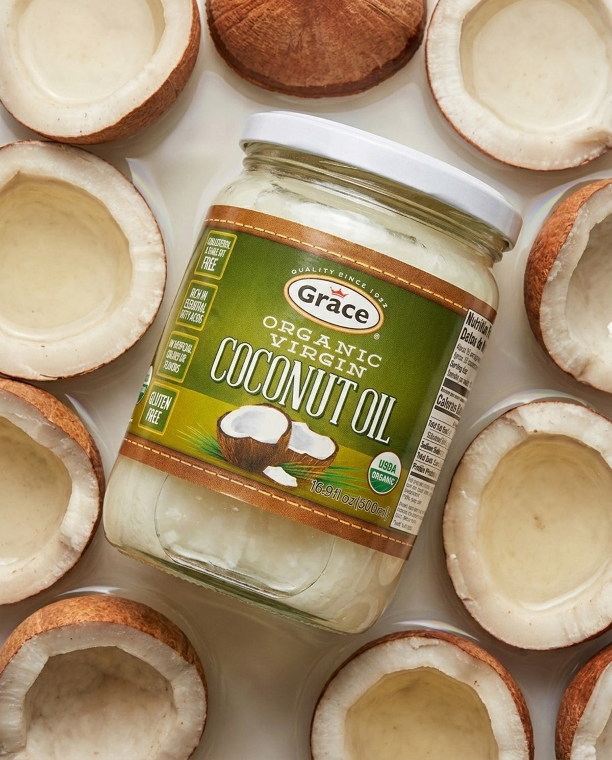 Angled view of Grace Organic Virgin Coconut Oil 500 mL jar showcasing its label among coconut halves