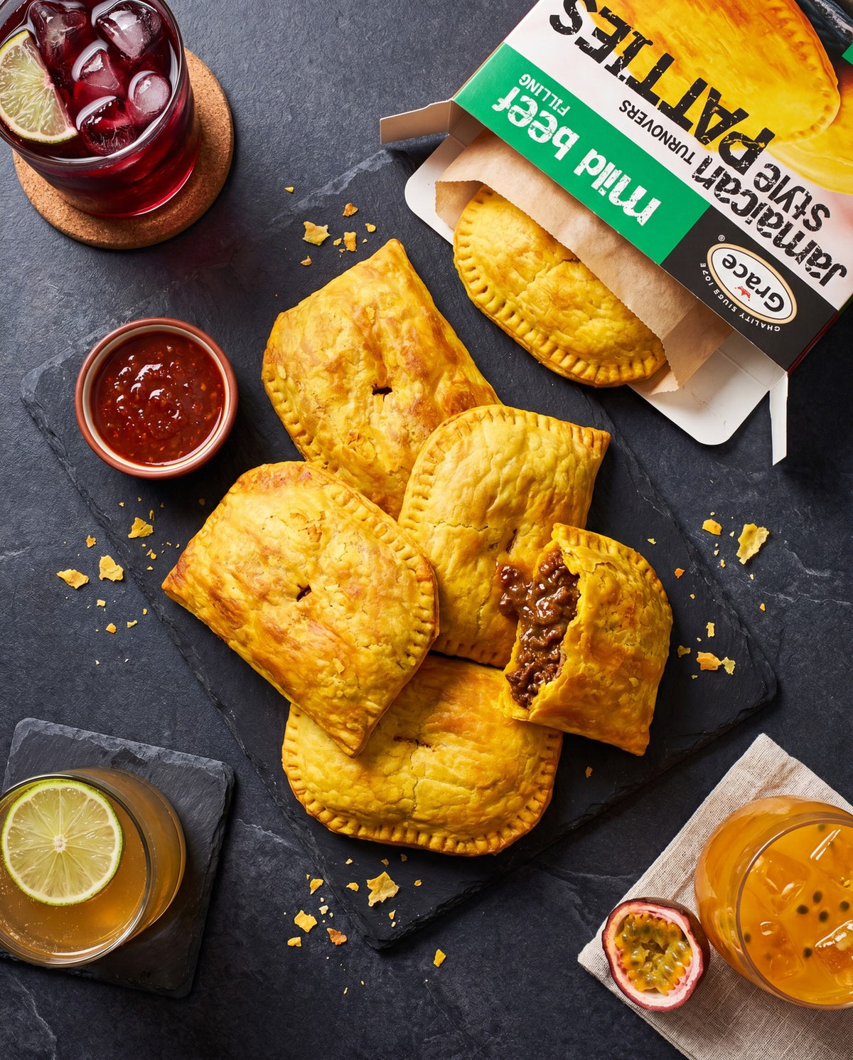 Overhead view of Grace Mild Beef Jamaican Style Turnover Patties with golden flaky crust, beef filling, and package on dark slate