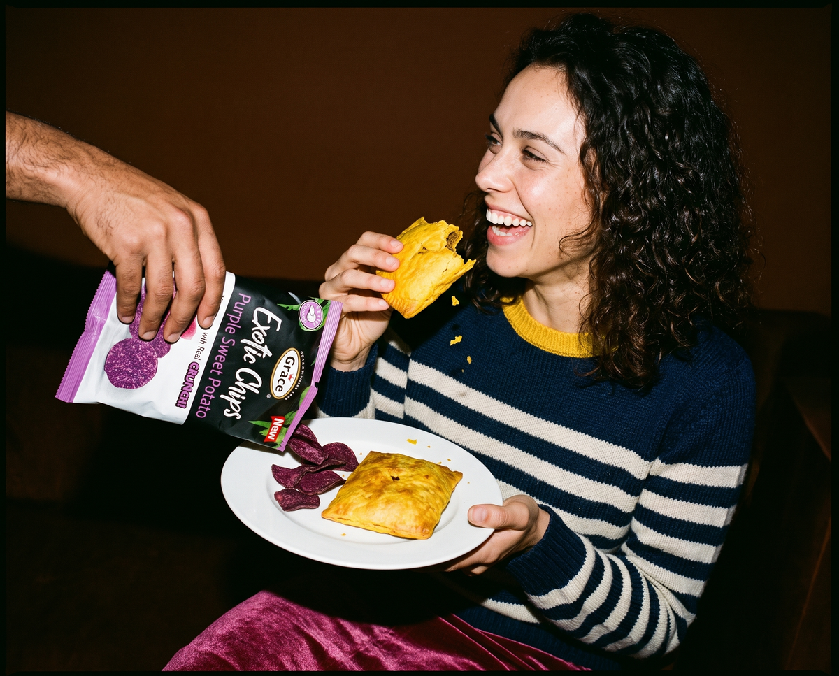 Woman enjoying a pastry as Grace Exite Chips Purple Sweet Potato are served, with snacks on a plate