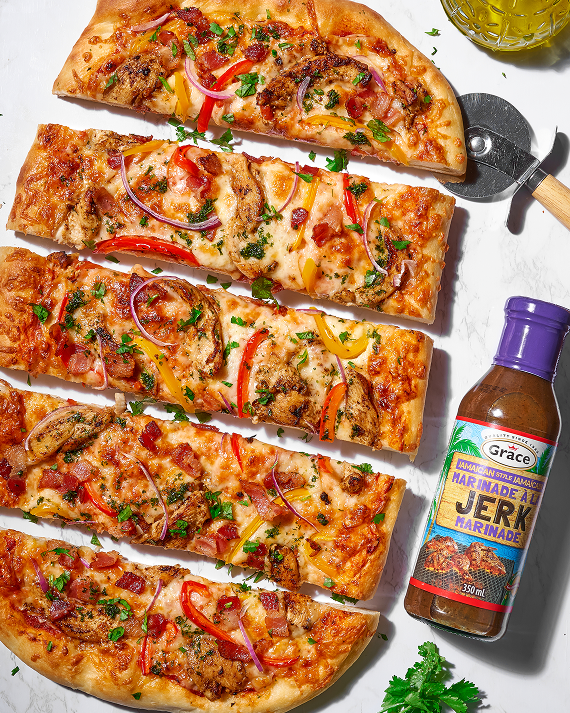 Grace Jamaican Jerk Marinade bottle beside sliced jerk chicken pizza on a marble surface with pizza cutter and parsley