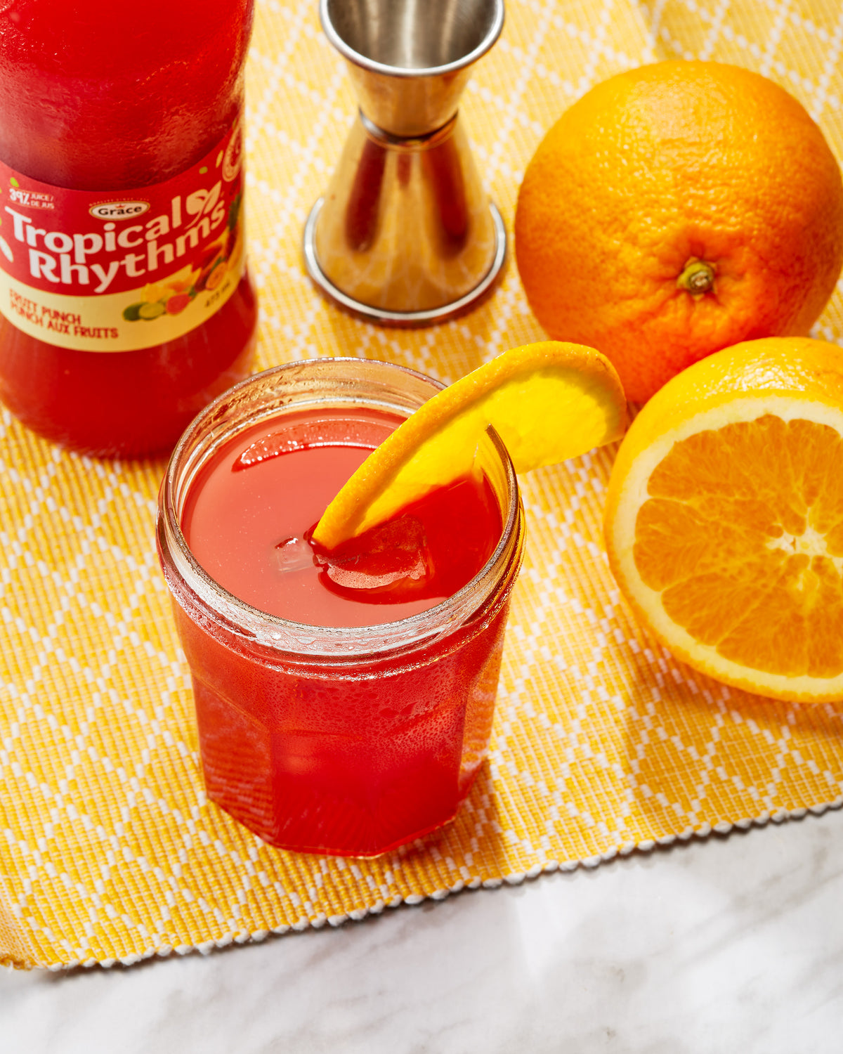 Top-down view of Tropical Rhythms fruit punch bottle and jar of red drink with orange slice on yellow placemat